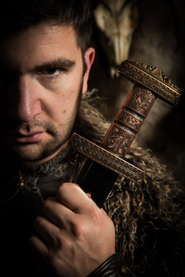 Studio portrait of Josh Martín in a fur cloak, holding an ornate Viking sword hilt